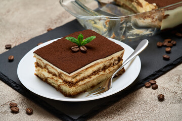 Traditional Italian Tiramisu dessert in glass baking dish and portion on grey concrete background
