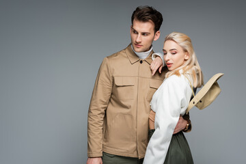 stylish man in jacket hugging blonde woman isolated on grey
