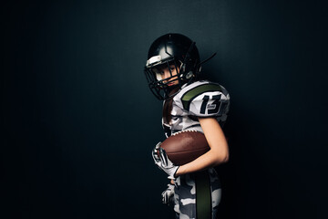 Athletic woman poses in American football uniform and helmet with ball.