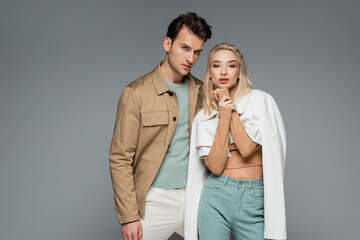 stylish models in pants and jackets posing isolated on grey