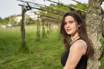 young long-haired girl sitting in a a vineyard. woman in white pants and black t-shirt resting in nature. light-skinned teenager walking through the plantations of a winery