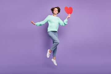 Fototapeta na wymiar Full length body size view of attractive cheerful girl jumping holding red heart card isolated over violet purple color background