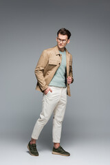 full length of stylish man posing with hand in pocket on grey