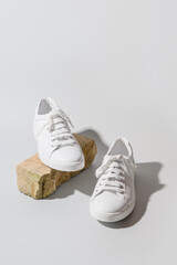 White women's new sneakers on a grey background and natural stone as stand. Vertical format. Close...