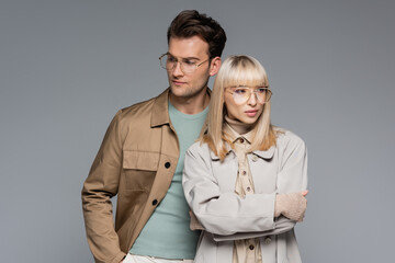 stylish couple in glasses posing and looking away isolated on grey