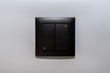 Black frame and button of the roller shutter switch up and down on gray wall in the house.