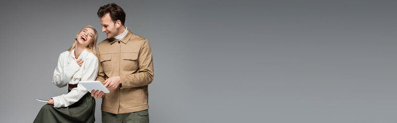 amazed woman holding smartphone near man with digital tablet isolated on grey, banner
