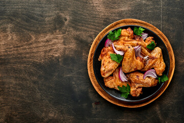 Grilled chicken wings or roasted bbq with spices and tomato salsa sauce on a black plate. Top view with copy space.
