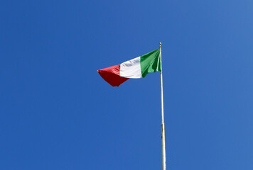 bandiera italiana che sventola sull'asta contro il cielo azzurro