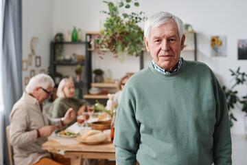 Portrait of senior man with grey hair looking at camera with his friends sitting at dining table in the background