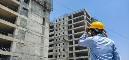 Rare view of a Young Asian male Engineer or Architect wearing Protective gears and looking at the buleprints of Building construction ongoing in the Construction site. Businessman. Finance. 