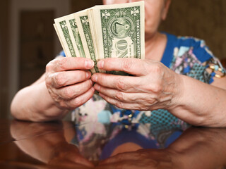 An elderly woman counts dollars. Last money for life, low incomes, poverty, 1 dollar bills.