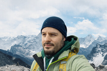 Man with backpack trekking in mountains. Cold weather, snow on hills. Winter hiking portrait