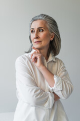 Mature woman with hand near chin posing isolated on grey