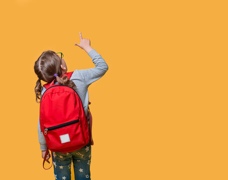 Back view of pupil in red backpack pointing up with the finger. childhood, education and people concept. happy smiling student girl with school bag go to school. Stylish kid. Child isolated on yellow