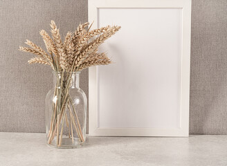 Blank white picture frame, vase with spike on the table.Beige wall background. Place for text.Cozy...