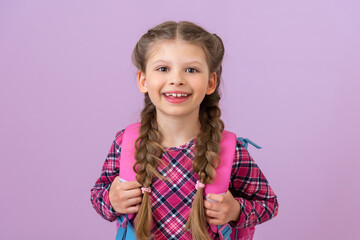 A little girl holds a school satchel and smiles against a pink isolated background.