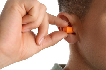 Man inserting foam ear plug on white background, closeup