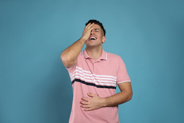Handsome man laughing on light blue background. Funny joke