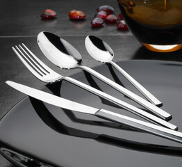 steel cutlery set on black elegant table  - obrazy, fototapety, plakaty
