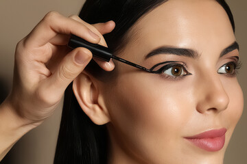 Fototapeta premium Artist applying black eyeliner onto woman's face on beige background, closeup