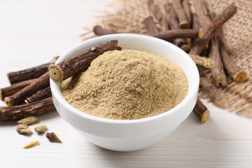 Powder in bowl and dried sticks of liquorice root on white table, closeup