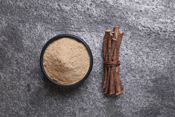 Powder in bowl and dried sticks of liquorice root on grey table, flat lay