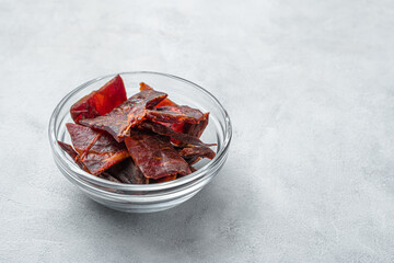 Jerky meat slices in a transparent cup on a light gray background with space to copy.