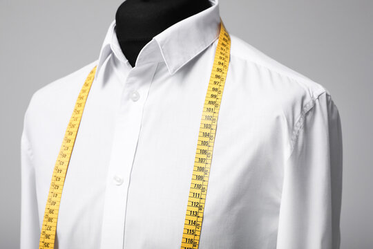 White shirt with tailor's measuring tape on mannequin against grey background, closeup
