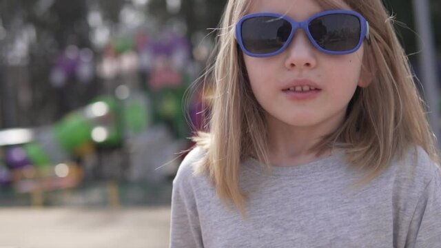 A little girl in sunglasses with symptoms of a cold walks outside in the spring, close-up. A child coughs in the street