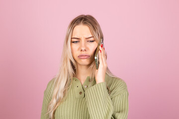 Pretty european woman in casual knitted sweater on pink background isolated hold phone having conversation with unhappy angry sad face