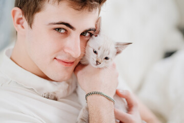 a young man holds a small white kitten and petting him. nevsky masquerade cat.