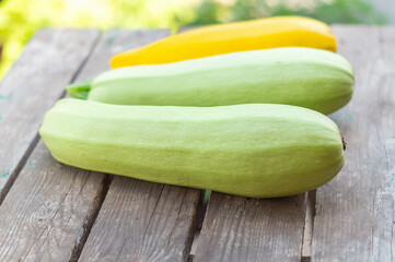Green zucchini lie in a row on a wooden oak table.  Fresh zucchini, illuminated by the sun, lie on a wooden surface in close-up. Healthy food background. Dietary and vegetarian food. Nature background