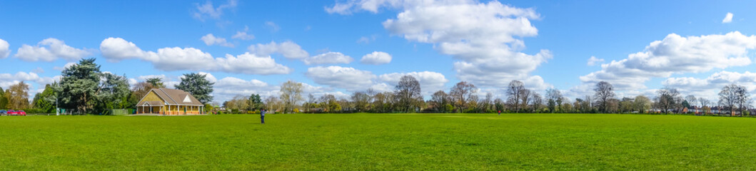 A panoramic view of Sol Joel Park, in Early, Reading, UK. An open green, public space on a day with. blue sky and clouds.
