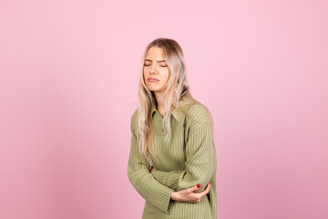 Pretty european woman in casual sweater on pink background suffering stomach ache with painful...