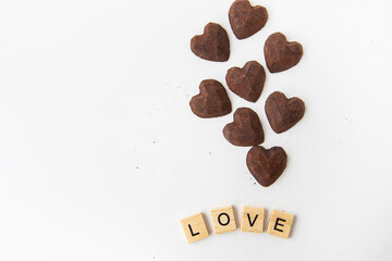 Truffle chocolate candies in the form of a heart on a white background. Inscription love made of wood letters. Place for an inscription.
