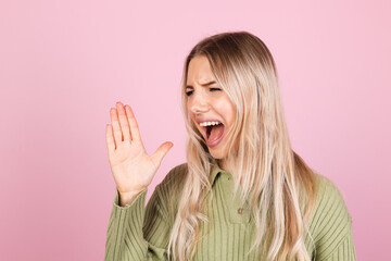 Pretty european woman in casual sweater on pink background shouting and screaming loud to side with hand on mouth. communication concept.