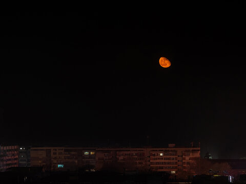 Rising large orange moon low in the sky over multi-storey residential buildings. View of the sleeping city at night.  Аstronomy, moon in the Wanning Gibbous phase. Moonrise over Varna. Night scene.