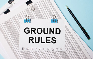 On a light blue background, documents, a pen and a sheet of paper on blue paper clips with the text GROUND RULES. Business concept.