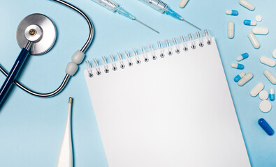 On a light gray background, a stethoscope, an electronic thermometer, pills, syringes and a...