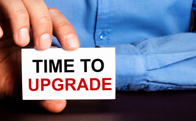 TIME TO UPGRADE is written on a white business card in a man's hand. Advertising concept