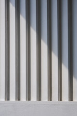 Sunlight and shadow on surface of white wooden sunshade battens on cement wall in vertical frame