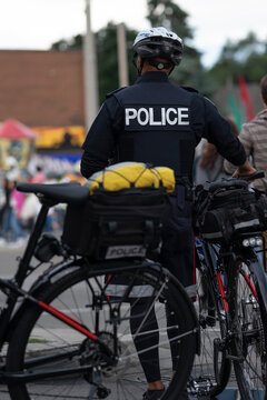 Bicycle Police Officer Standing Next To His Bike On A City Street. Essential Services Workers. Selective Focus. Toronto, Ontario, Canada.