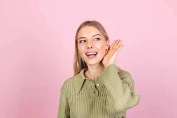Pretty european woman in casual sweater on pink background curious try to hear what you saying with...