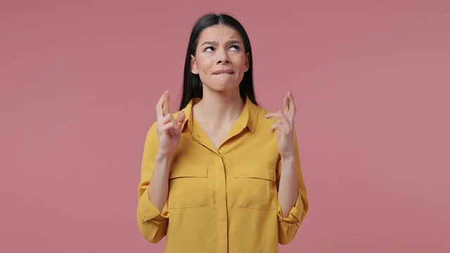 Pleading young latin woman in yellow shirt isolated on pink background studio. People lifestyle concept. Hold hands folded in prayer gesture keeping fingers crossed begging about something making wish