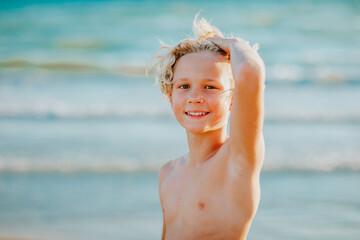 Portrait of cute teen boy with blond hair posing against the sea.
