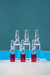 Glass ampoules with a solution of red and transparent for the treatment of diseases are on a blue background. Bottles for dilution and injections.