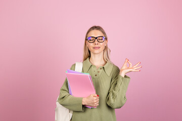 Pretty european woman in casual sweater on pink background with notebooks showing ok gesture education concept