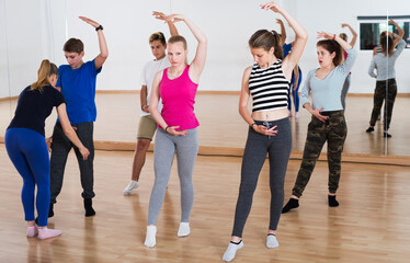 Fototapeta na wymiar Group of teenage boys and girls rehearsing ballet dance in dance hall