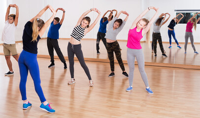 Fototapeta na wymiar Group of teenage students with female trainer stretching at dance class
